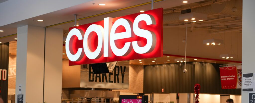 A photograph of the shop front of a Coles Supermarket showing the Coles sign lit up